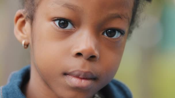 Close-up pensive little girl african american child raises head looking at camera front view sad baby outdoors portrait unsmiling schoolgirl beautiful unemotional face of lonely cute kid bored look — Wideo stockowe