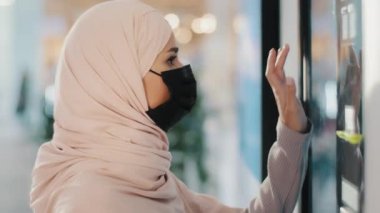 Koruyucu tıbbi maske takan genç Arap kadın self servis makinesinin yanında duruyor. Müslüman kız alışveriş siparişleri alıyor. Bakkaldan servis için ödeme yapılıyor.