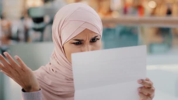 Close-up jonge moslim vrouw zitten lezen papier brief slecht nieuws gefrustreerd islamitisch meisje geschokt door informatie financiële moeilijkheden faillissement kennisgeving ontslag voelt jammer verdriet irritatie — Stockvideo