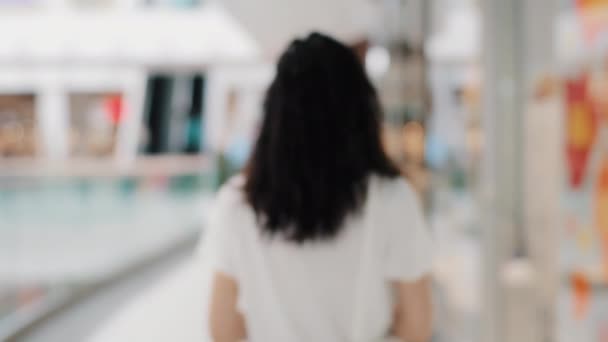 Out of focus blurred background back view young curly brunette girl walking indoors in public place supermarket shopping center weekend moving woman shopper consumer looking sale in clothing store — Vídeo de Stock