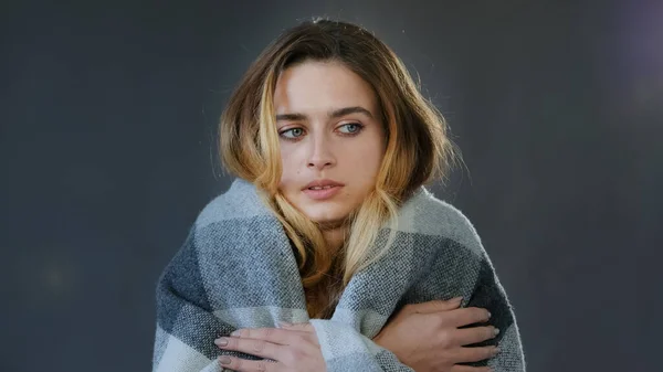 Female portrait in studio on gray background young beautiful woman blonde girl model lady wrapped in plaid blanket feels cold chills get sick low temperature needs warmth suffers from feeling unwell — Stock fotografie