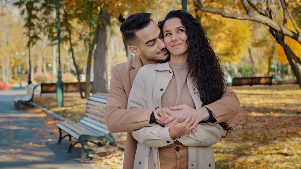 Chico hispano abraza novia de la espalda pareja enamorada divertirse comunicarse mirando a la distancia discutir conjunto futuro en otoño parque joven familia abrazando sentirse feliz al aire libre romántico fecha concepto — Foto de Stock