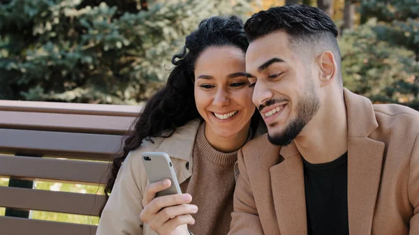 İspanyol çift, Autumn Park 'ta bankta oturuyor. Genç adam telefonda adam ve kız sohbeti yapıyor. Ekran cihazına bakın. — Stok fotoğraf