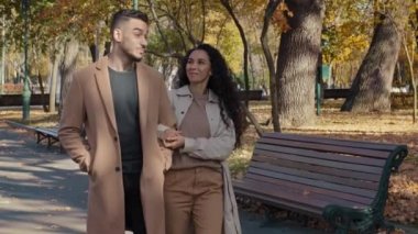 Young family walking in autumn park enjoying pleasant conversations on romantic date girl holding guy hand happy couple spend carefree weekend together outdoors hispanic man and woman joyfully smiling