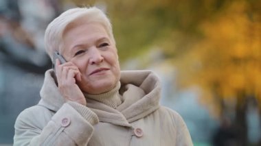 Close-up elderly lady speak on smartphone shares news grandma enjoying using device outdoors positive aged woman smiling talking with children by telephone in autumn park remote communication concept