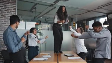 Hispanic businesswoman dancing on table employees have fun conference room celebrating corporate success female leader with colleagues enjoy office party happy diverse business people rejoice victory