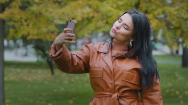 Yakın plan İspanyol bir kadın, elinde telefonuyla, elinde cep telefonuyla gezici kız blogcuya poz veriyor. Akıllı telefonlu kadın vlogger 'ı kullanarak blog için fotoğraf çekiyor.