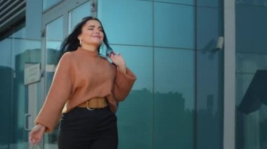Happy young stylish woman shopper walking street holding bright gift bags in hands hispanic overweight girl walks whirls smiling rejoices new purchases bought on sale enjoy discounts at mall store