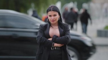 Close-up confident businesswoman stands on street near roadway arms crossed over chest successful beautiful girl staring intently at camera woman in business suit posing while standing at crosswalk