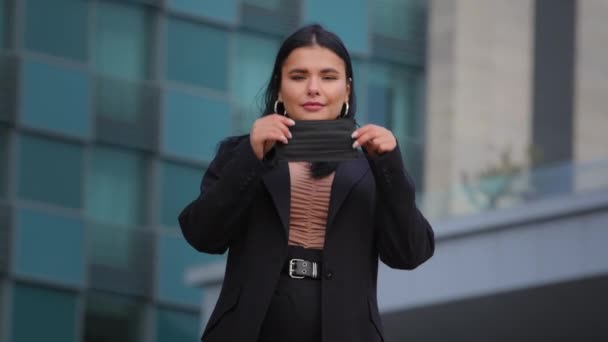 Fiatal spanyol lány áll a város épületében háttér nézi kamera üzletasszony visel orvosi védő maszk védi az egészséget a vírusos fertőzéstől világjárvány légszennyezés karantén — Stock videók