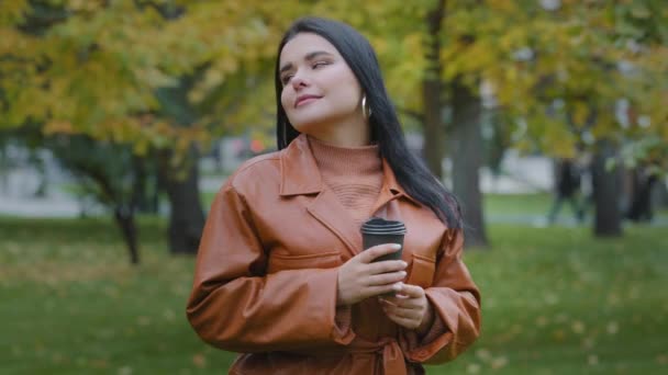 Close-up young hispanic woman smiling drinking coffee from disposable cup outdoors in autumn park dreamy brooding overweight girl enjoying fragrant hot drink on cloudy day break during working hours — Wideo stockowe