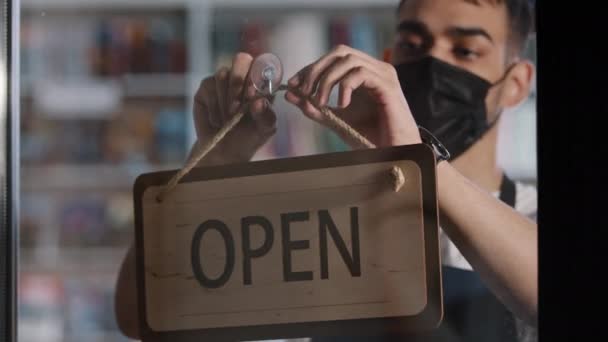 End of working day close-up tired young male salesman barista waiter wearing medical mask closes shop cafe cafeteria restaurant hispanic man turns wooden sign that says CLOSED on glass door goes away — Stock Video