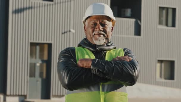 Primo piano anziano afro-americano operaio edile in piedi in casco protettivo uniforme all'aperto fiducioso lavoratore incrociato le braccia attraverso petto costruttore appaltatore di successo in cerca di fotocamera posa — Video Stock