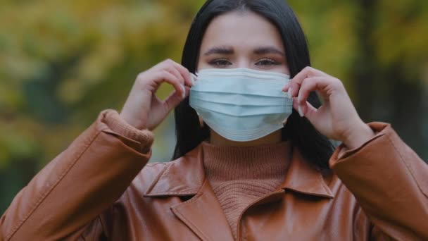 Close-up young woman stands outdoors in park takes off medical protective mask from face throw respirator smiling hispanic girl inhales deeply Fresh air enjoys freedom end quarantine pandemic over — стоковое видео