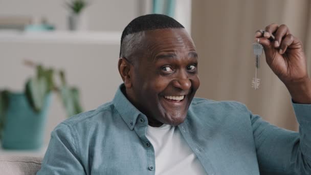 Close-up happy adult african american man sitting looking at camera showing bunch of keys from new purchased or rented apartment mature male smiles enjoys buying house shows sign of approval thumbs up — Wideo stockowe