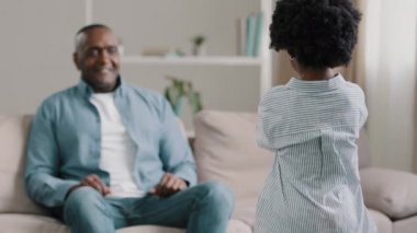 African american family mature dad sitting at home on couch surprised accepting birthday greetings little loving daughter gives handmade card for fathers day child comes to happy man hugs tightly