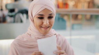 Happy young arab woman reading paper letter smiling enthusiastic muslim girl rejoices of good news entered university exam results bank loan approval salary increase career advancement got dream job