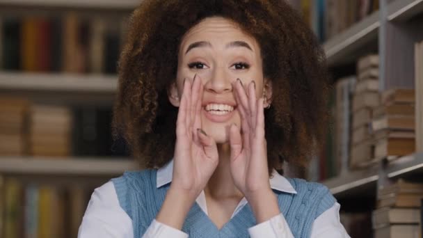 Close-up young woman indoors speaks quietly covering mouth hands telling confidential information secret african american girl student showing silence gesture brings finger to lips forbids speaking — Wideo stockowe