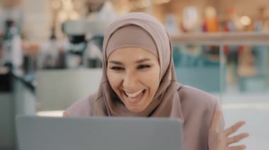 Close-up young muslim woman in hijab sitting with laptop rejoicing in victory excited girl winner celebrating success happy arab female reads good news gets dream job bank loan approval lottery win