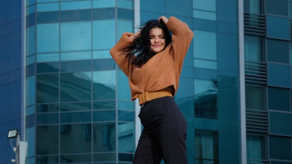 Happy carefree young woman brunette model actively dancing outdoors on city building background funny joyful hispanic girl student smiling rhythmically moving winner dance enjoying weekend freedom — Zdjęcie stockowe