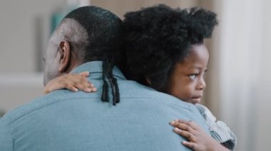 Happy african american kid girl hugging beloved father unrecognizable adult man sits with back to camera holding child in arms daughter and dad cuddling unconditional love tight hug cuddle embrace