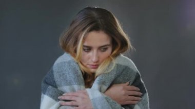 Female portrait in studio on gray background young beautiful woman blonde girl model lady wrapped in plaid blanket feels cold chills get sick low temperature needs warmth suffers from feeling unwell