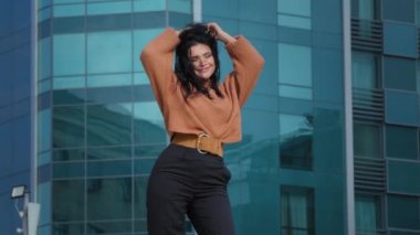 Happy carefree young woman brunette model actively dancing outdoors on city building background funny joyful hispanic girl student smiling rhythmically moving winner dance enjoying weekend freedom