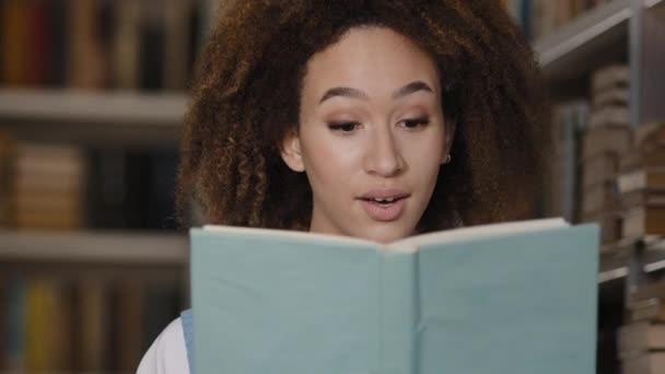 Close-up Africano americano menina estudante escondido atrás de livro de leitura livro emocional jovem mulher fica na biblioteca atentamente lê romance surpreendido chocado com sentimento final inesperado perplexo — Vídeo de Stock