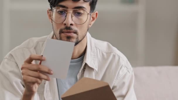 Primer plano árabe hombre barbudo chico con gafas sentado en casa en el interior recibe sobre con malas noticias preocupante problema sosteniendo la cabeza tristeza triste tarjeta postal triste con rechazo deuda banco aviso pérdida concepto — Vídeo de stock