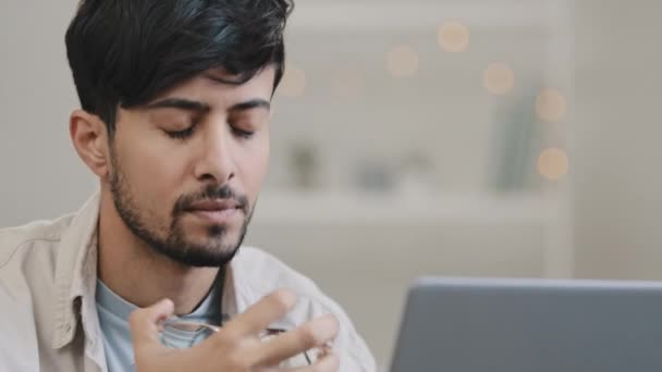 Close-up male face arabic hispanic man bearded guy working with laptop feels stress suffering from headache takes off glasses rubs eyes worried about business problems pressure migraine difficult task — Αρχείο Βίντεο