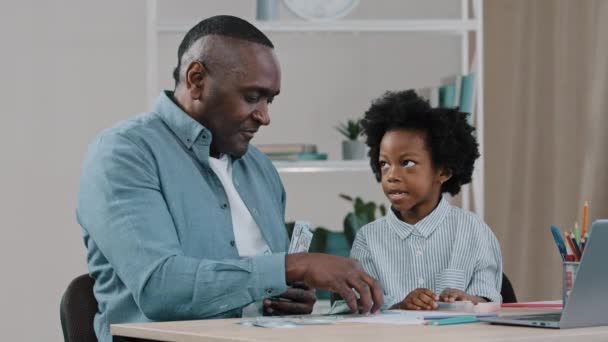 Vuxen afrikansk amerikansk far lär sig att räkna liten dotter hem skolgång mogen man lära barn flicka aritmetik visar papper pengar kontanter dollar lärande medan du spelar barn och pappa spela kul — Stockvideo