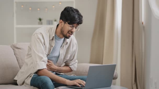 Joven hombre de negocios freelance en casa trabajando con el ordenador portátil siente dolor abdomen molestias diarrea problemas hepáticos apendicitis síntomas indigestión espasmo estomacal dolor sufre de envenenamiento enfermedad — Vídeo de stock