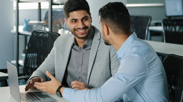 Two Arab male businessmen satisfied with result of negotiations concluded contract. Indian employees sitting in modern office using laptop receiving good news, young colleagues discussing project — Stockfoto