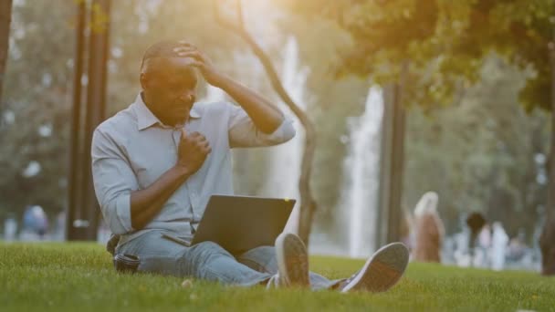 Focused elderly African american businessman entrepreneur sitting on grass in city park working on computer, feeling tired stressed rubbing massaging neck, suffering from pain or stiff muscles concept — Stockvideo