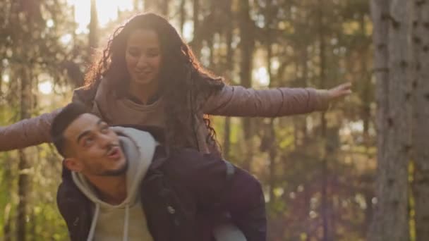 Multinational couple newlyweds, Hispanic woman and arabic man walking having fun in autumn forest. Young guy carries millennial girl on her back playing. Happy lifestyle family outdoor recreation — Vídeo de Stock