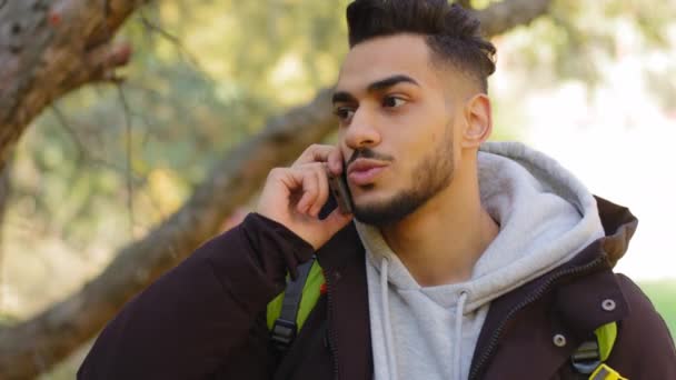 Hezký vousatý hispánec mluví na mobilním telefonu v lese stromy pozadí, tisíciletý arabský chlap zvedá hovor rozhovory s chytrým telefonem konverzace pomocí bezdrátového mobilu v lese venku — Stock video