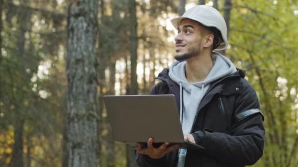 Taking measures for reforestation of woodlands. Millennial Indian man forestry engineer in hardhat with laptop in woods working and supervising in park, watching of wildlife sanctuary checking trees — Video Stock