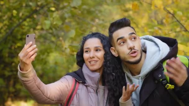 Couple of diverse young travelers walking in autumn forest, making video call, millennial travel bloggers chatting live, using smartphone looking at camera, waving hands, spending time together — Vídeo de Stock