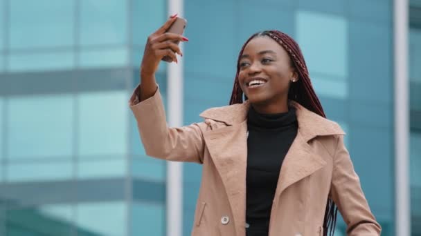 Happy successful young african american woman standing outdoor on modern building background, making video call using smartphone. Smiling student girl, female office employee has pleasant conversation — Stok video