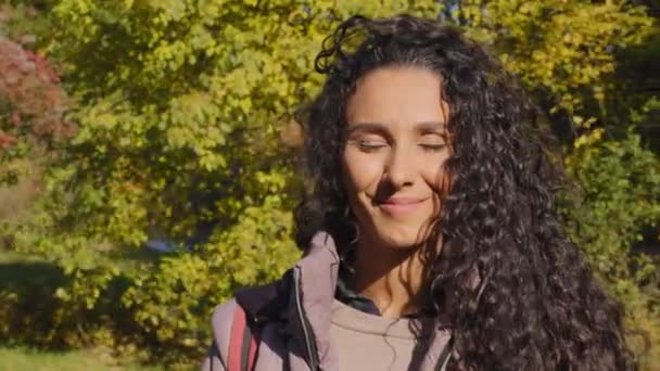 Pretty millennial hispanic woman looking at camera with white-toothed smile standing at green forest trees background. Happy girl student fixes curly long hair, young beautiful lady closeup portrait — Stok video