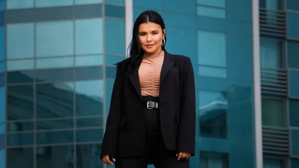 Ung latinamerikansk affärskvinna anställd företag står tryggt utomhus på bakgrund kontor byggnad tittar på kameran poserar i framgångsrik pose känns nöjd med karriärutveckling främjande — Stockfoto