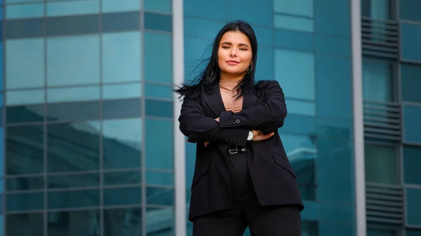 Ung latinamerikansk affärskvinna anställd företag står tryggt armarna korsas utomhus på bakgrund kontor byggnad tittar på kameran poserar i framgångsrik pose känns nöjd med karriärutveckling — Stockfoto
