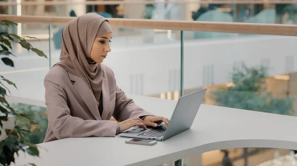 Fokuserade allvarliga arabiska affärskvinna professionell entreprenör sitter på kontoret skrivbord skriva tittar på bärbar skärm studera online kurs muslim flicka frilansare fungerar på distans med hjälp av dator enhet — Stockfoto