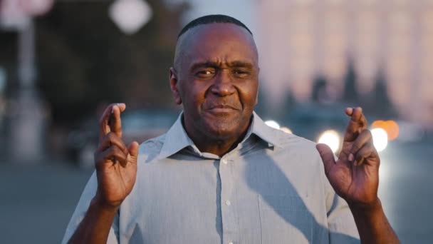Der Mensch hofft auf Wunder, der Verzweifelte auf Geste. Hoffnungsvoller älterer afroamerikanischer Geschäftsmann drückt mit geschlossenen Augen die Daumen, wünscht sich nach draußen und fleht um Hilfe — Stockvideo