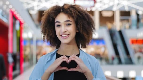 Detailní úsměv kudrnaté mladé milující druh jemný africký Američan žena dívka dobrovolník přítelkyně při pohledu na kameru ukazuje charita láska gesto pomoc laskavost dělá srdce tvar s rukama romantické znamení — Stock video