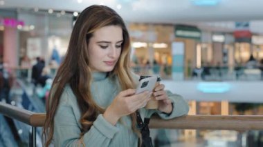 Beyaz kadın milenyum kızı alışveriş merkezinin iş yerinde cep telefonuna bakıyor akıllı telefondan mesaj yazıyor kağıt bardaktan kahve içen kablosuz internet uygulaması kullanıyor.