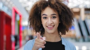 İçerideki kadın portresi. Mutluluktan memnun Afro-Amerikan kıvırcık kadın. Kameraya işaret parmağıyla işaret parmağıyla el telefonu tutuyor.