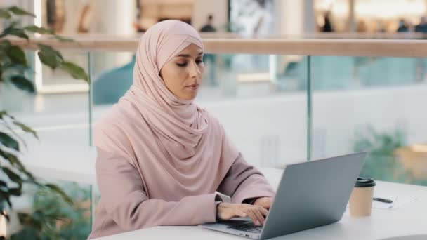 Серьёзная арабская женщина в хиджабе, работающая удалённо, печатая на ноутбуке, пишет статью о писательнице-мусульманке журналистке, студентке, творческой личности, погружённой в мысли в ожидании вдохновения — стоковое видео