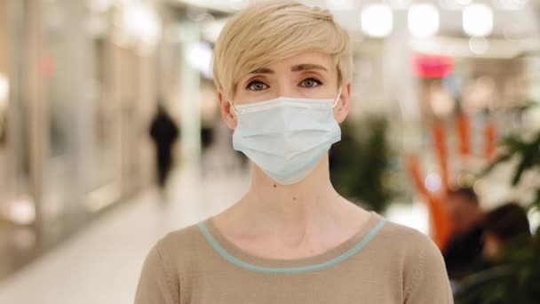 Orta yaşlı, kısa saçlı bir iş kadını portresi. 40 'lı yaşlarda, yetişkin bir kadın, tıbbi koruyucu maske takıyor. Alışveriş merkezindeki Coronavirus pandemisi hastası Covid19' a bakıyor. — Stok video