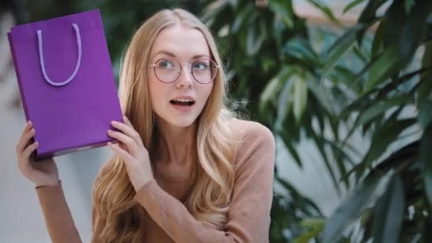 Porträt aufgeregt junge Frau mit Brille schüttelt Geschenktüte erstaunlich kaukasischen Millennial Geburtstagskind öffnet lila Paket fühlt Freude Zufriedenheit Blondine lächelt glücklich tanzen genießen Überraschung — Stockvideo